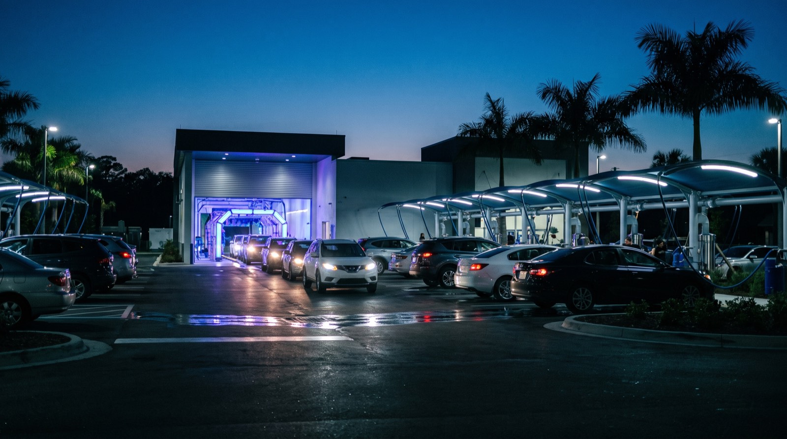 Illustrative image, not the actual property. Cars lining up at a lit express car wash tunnel with covered vacuum stations and palm trees at dusk